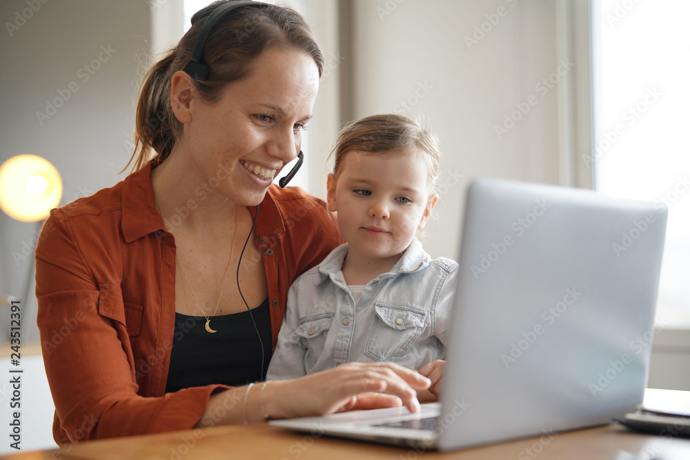 Mother working from home on computer with her young daughter Mother working from home on computer with her young daughter
