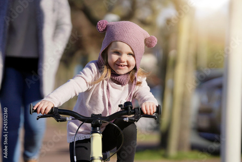 Adorable young girl in wooly hat riding bike outdoors © goodluz