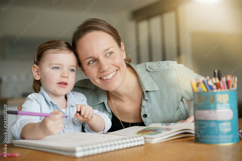 Mother and young daughter drawing and reading together at home Mother and young daughter drawing and reading together at home
