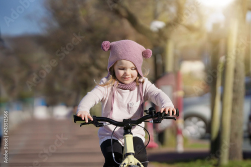 Adorable young girl in wooly hat riding bike outdoors