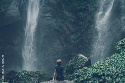 Young woman posing on a great Sekumpul waterfall in the deep rainforest of Bali island, Indonesia.
