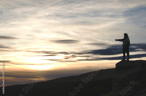 Man climbed on a rock in the heights in a mountainous landscape at sunset
