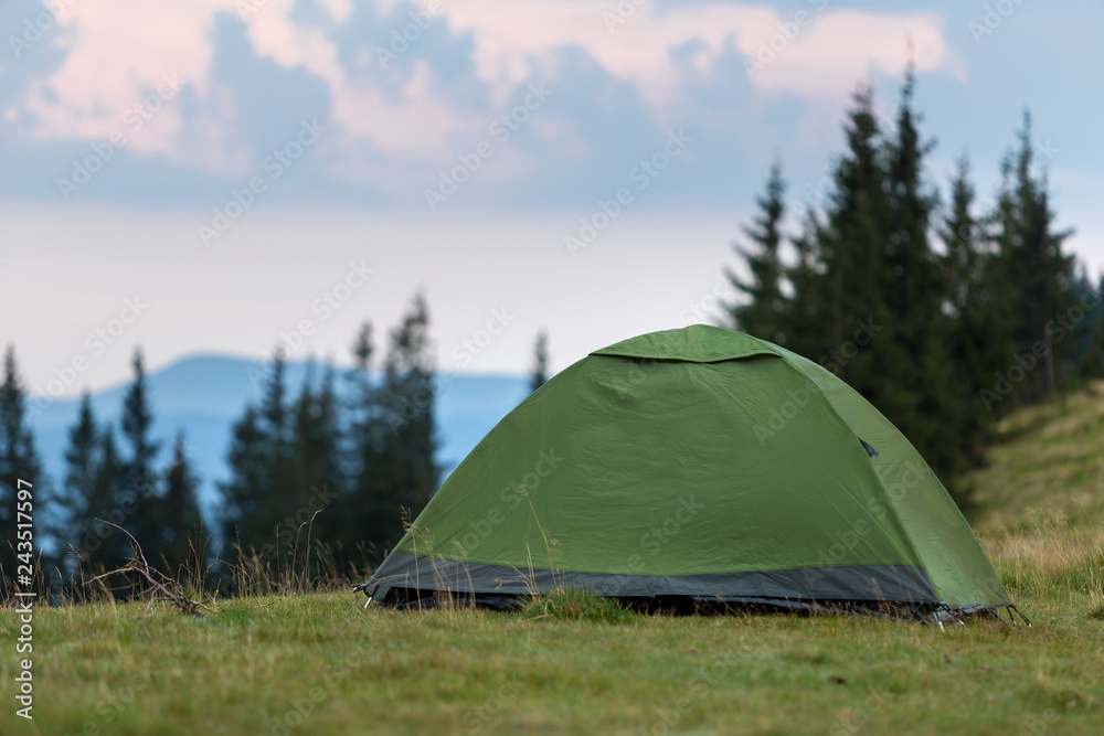 Small tourist tent on grassy mountain hill. Summer camping in mountains at dawn. Tourism concept.