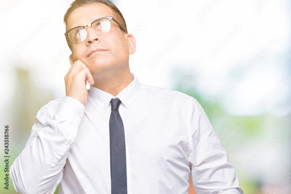 Middle age bussines arab man wearing glasses over isolated background with hand on chin thinking about question, pensive expression. Smiling with thoughtful face. Doubt concept.