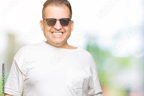 Middle age arab man wearig white t-shirt and sunglasses over isolated background with a happy and cool smile on face. Lucky person. © Krakenimages.com