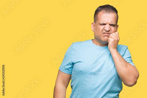 Middle age arab man wearing blue t-shirt over isolated background looking stressed and nervous with hands on mouth biting nails. Anxiety problem.