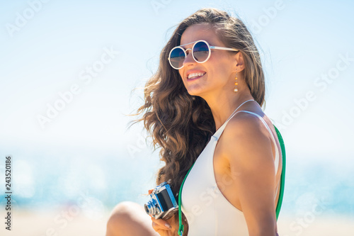 woman with retro photo camera looking into distance on beach
