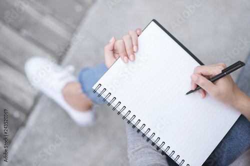 Fotografie Top view female hands with pen writing on notebook notepad sitting in public park outdoor