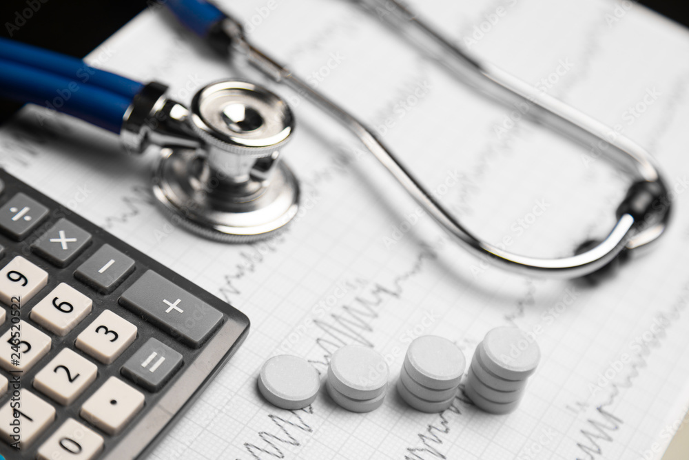 Stethoscope, pills and calculator are on a sheet with an electrocardiogram Stethoscope, pills and calculator are on a sheet with an electrocardiogram