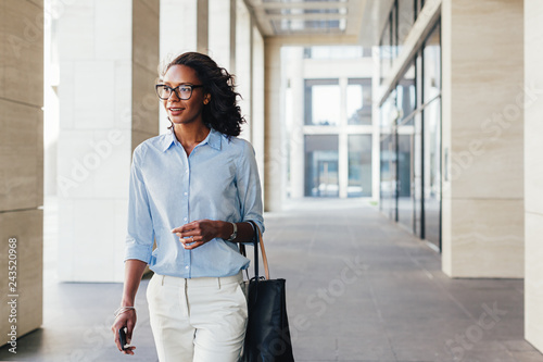 Female business professional walking outside an office building with bag on a hand photo