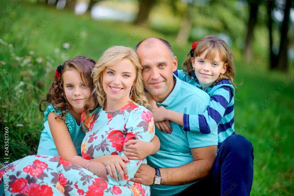 Fototapeta premium happy family resting in nature sitting on the grass hugging and laughing