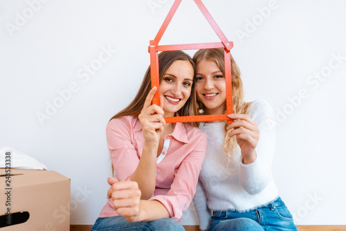 Two women having rented a new apartment moving in looking thru folding rule photo