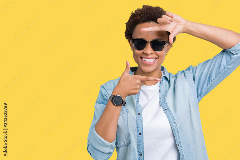 Obraz premium Beautiful young african american woman wearing sunglasses over isolated background smiling making frame with hands and fingers with happy face. Creativity and photography concept.