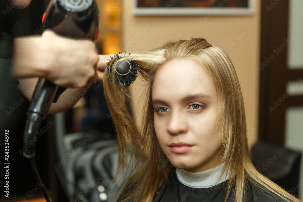 Fototapeta premium Professional hairdresser dyeing hair of her client in salon. Haircutter dry hair with hairdrier. Selective focus.