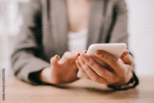 cropped view of businesswoman using smartphone in office