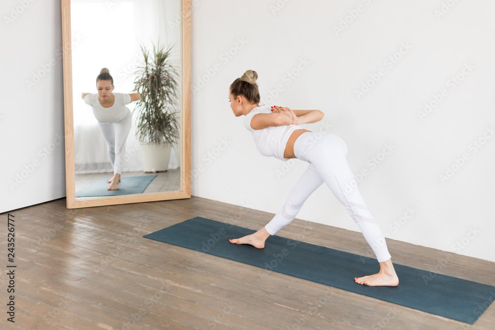 Sporty young woman doing yoga practice on white background at home.
