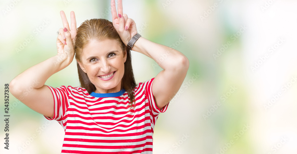 Middle age mature woman wearing casual t-shirt over isolated background Posing funny and crazy with fingers on head as bunny ears, smiling cheerful