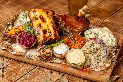 The concept of European cuisine in the Czech restaurant. Dish on the big company on a wooden board. Sauerkraut, pickled cabbage, sauce for meat in onions, pork knuckle and tenderloin.