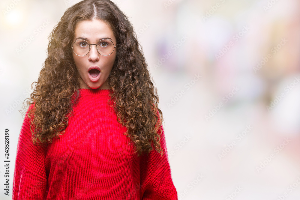 Beautiful brunette curly hair young girl wearing glasses and winter sweater over isolated background afraid and shocked with surprise expression, fear and excited face. Beautiful brunette curly hair young girl wearing glasses and winter sweater over isolated background afraid and shocked with surprise expression, fear and excited face.