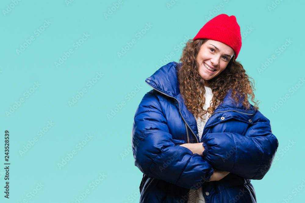 Beautiful young brunette curly hair girl wearing winter coat, wool cap and sweater over isolated background happy face smiling with crossed arms looking at the camera. Positive person.
