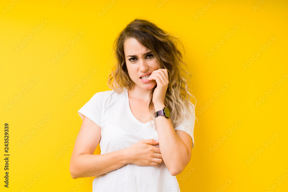 Young beautiful blonde woman over yellow background looking stressed and nervous with hands on mouth biting nails. Anxiety problem. Young beautiful blonde woman over yellow background looking stressed and nervous with hands on mouth biting nails. Anxiety problem.