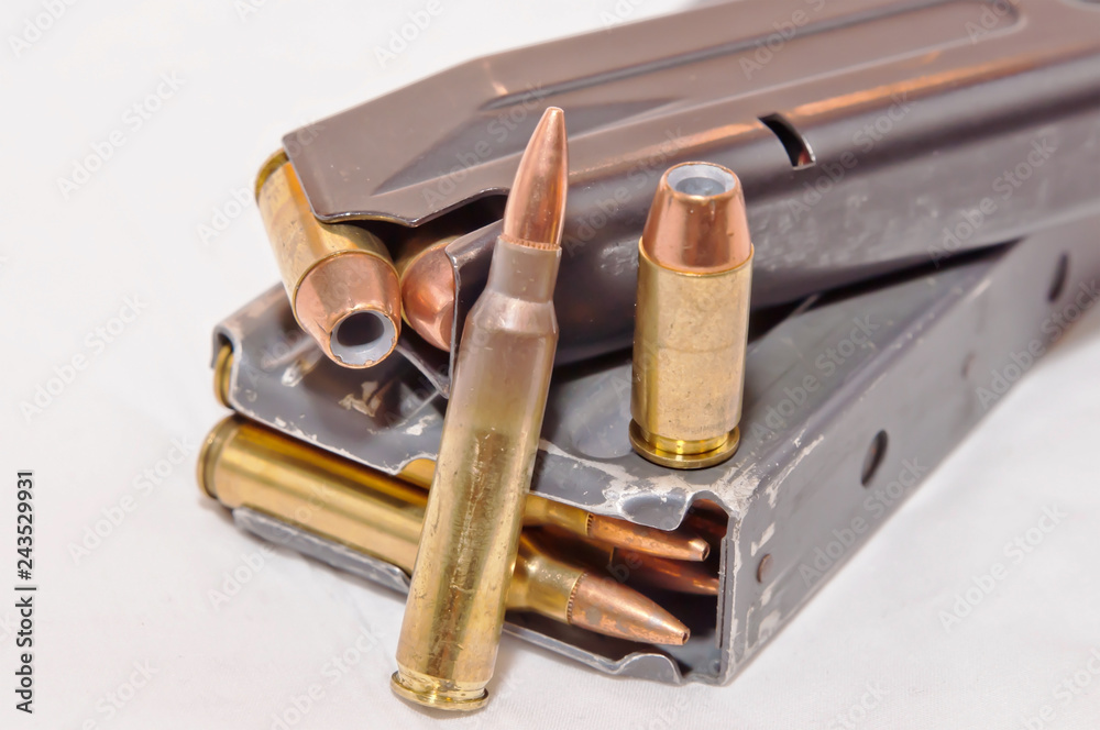 A loaded handgun magazine with 40 caliber bullets and a loaded rifle magazine with .223 caliber bullets along with each of those bullets on the magazines on a white background
