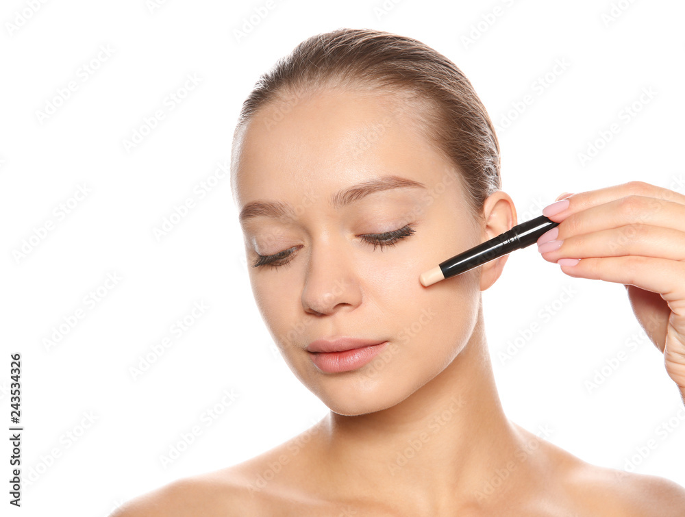 Young woman applying foundation on her face against white background