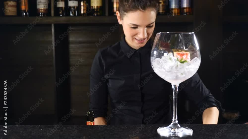 Girl bartender in black uniform putting a strawberry in glass with ice cubes preparing cocktail. Happy bartender concept. 4k Girl bartender in black uniform putting a strawberry in glass with ice cubes preparing cocktail. Happy bartender concept. 4k