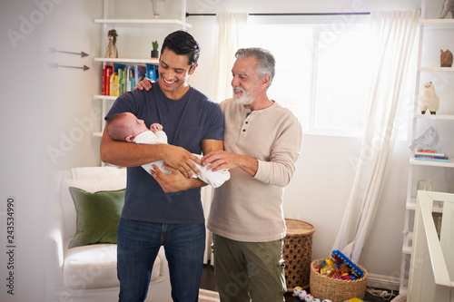 Proud senior Hispanic man standing with his adult son holding his four month old boy photo