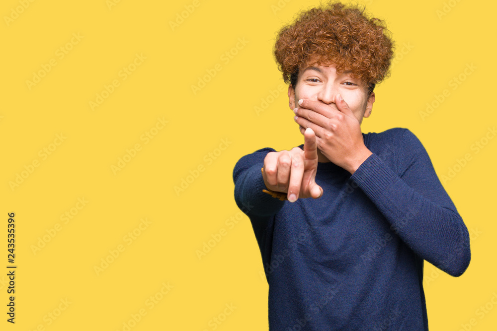 Young handsome man with afro hair Laughing of you, pointing to the camera with finger hand over mouth, shame expression Young handsome man with afro hair Laughing of you, pointing to the camera with finger hand over mouth, shame expression