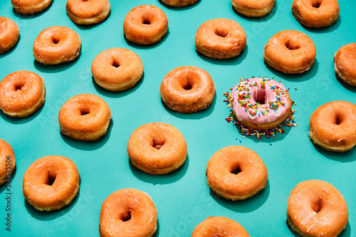 one pink donut with sprinkles in a lineup of glazed donuts