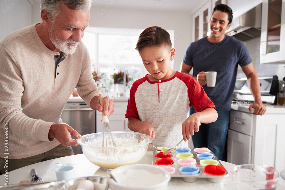Dad watching his son making cakes with grandad at the kitchen table, close up Dad watching his son making cakes with grandad at the kitchen table, close up