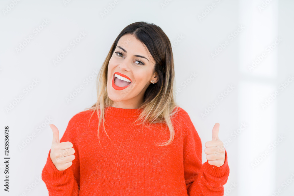 Young woman wearing casual red sweater over isolated background success sign doing positive gesture with hand, thumbs up smiling and happy. Looking at the camera with cheerful expression Young woman wearing casual red sweater over isolated background success sign doing positive gesture with hand, thumbs up smiling and happy. Looking at the camera with cheerful expression