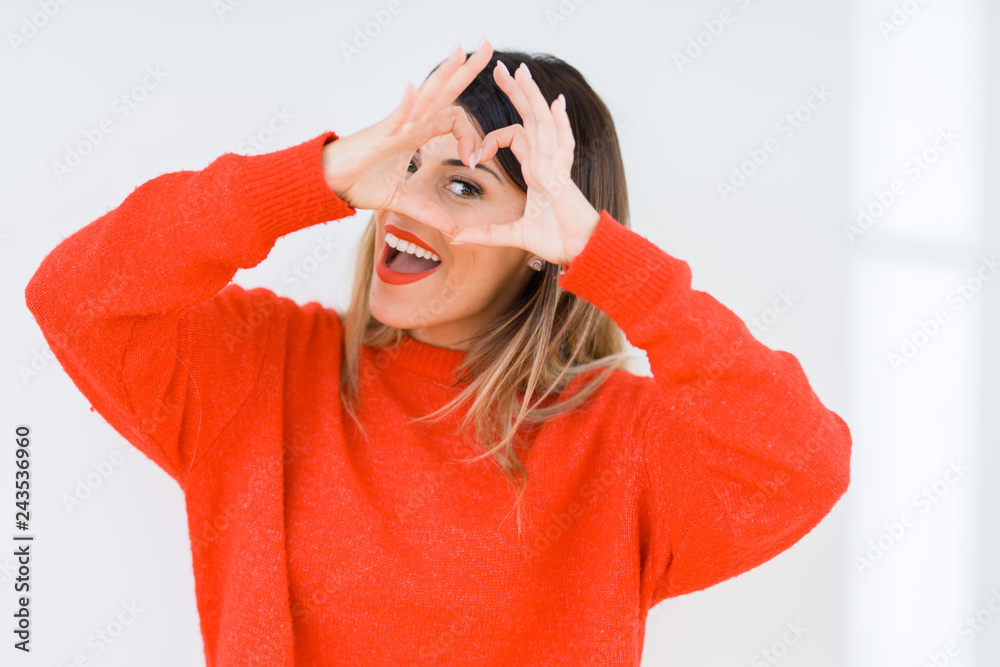 Young woman wearing casual red sweater over isolated background Doing heart shape with hand and fingers smiling looking through sign Young woman wearing casual red sweater over isolated background Doing heart shape with hand and fingers smiling looking through sign