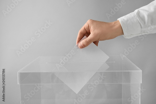 Man putting his vote into ballot box on light background, closeup