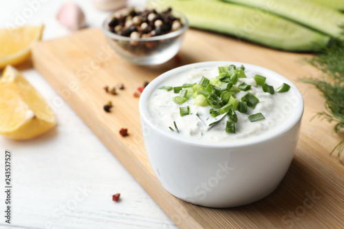 Ceramic bowl of cucumber sauce with ingredients on wooden table, space for text. Traditional Tzatziki