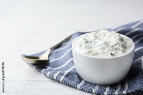 Cucumber sauce in ceramic bowl and spoon on wooden background, space for text. Traditional Tzatziki