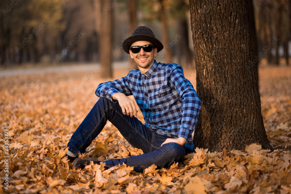 Fashion outdoor portrait of young happy man with hat and sunglasses in fall, retro style color tones. Male fashion. Fashion outdoor portrait of young happy man with hat and sunglasses in fall, retro style color tones. Male fashion.