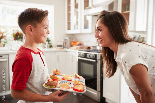 Pre-teen Hispanic boy presenting the cakes he has baked to his proud mother, close up