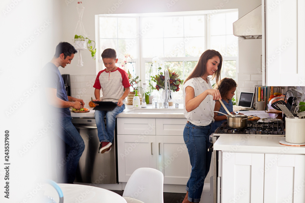 Mother and young daughter preparing food at hob in kitchen, pre-teen son and dad in the background Mother and young daughter preparing food at hob in kitchen, pre-teen son and dad in the background
