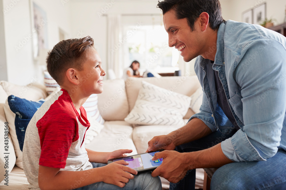 Fototapeta premium Pre-teen boy and dad playing a game on a tablet computer in the sitting room, close up