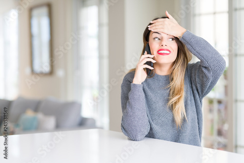 Young beautiful woman talking on the phone at home stressed with hand on head, shocked with shame and surprise face, angry and frustrated. Fear and upset for mistake.