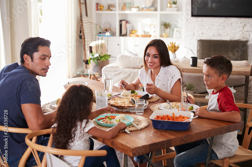 Young Hispanic family sitting at dining table eating dinner together