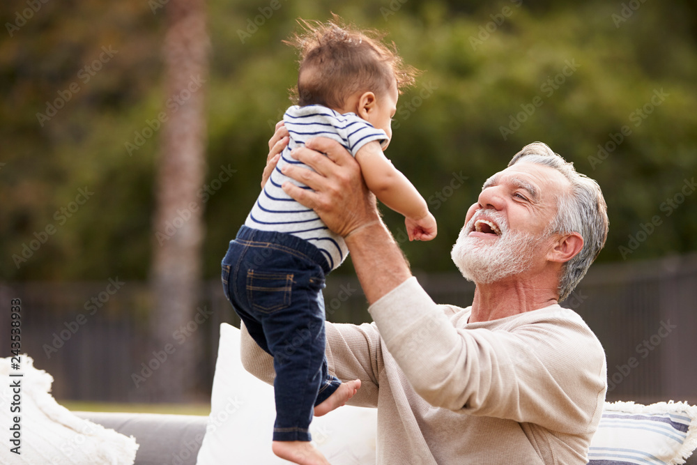 © Monkey Business - Senior Hispanic man sitting in the garden lifting his baby grandson in the air and smiling to him