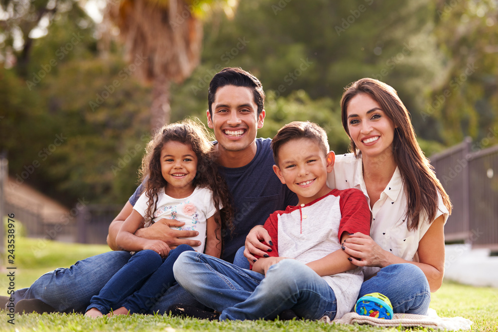 Fototapeta premium Happy young Hispanic family sitting the on grass in the park smiling to camera, close up
