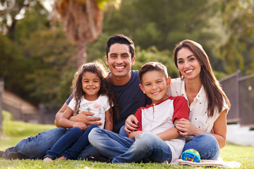 Happy young Hispanic family sitting the on grass in the park smiling to camera, close up