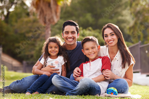 Happy young Hispanic family sitting the on grass in the park smiling to camera, close up