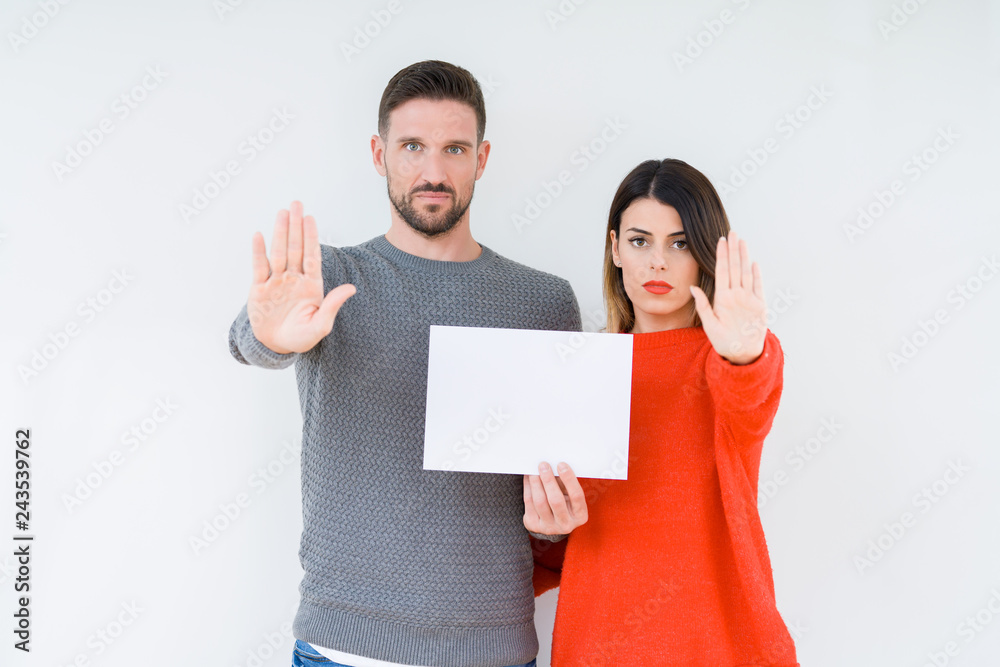 Young couple holding blank sheet paper over isolated background with open hand doing stop sign with serious and confident expression, defense gesture Young couple holding blank sheet paper over isolated background with open hand doing stop sign with serious and confident expression, defense gesture