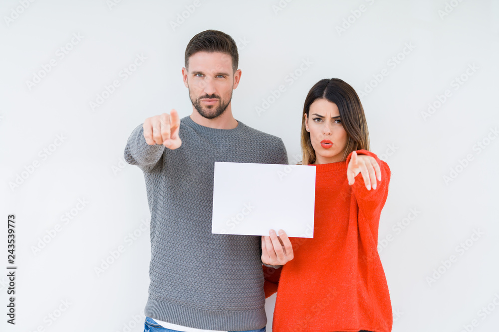 Young couple holding blank sheet paper over isolated background pointing with finger to the camera and to you, hand sign, positive and confident gesture from the front Young couple holding blank sheet paper over isolated background pointing with finger to the camera and to you, hand sign, positive and confident gesture from the front