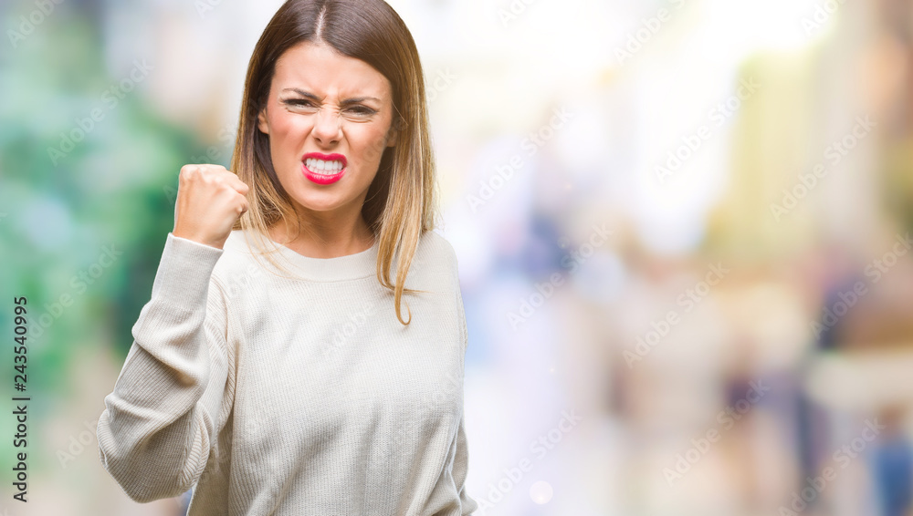 Young beautiful woman casual white sweater over isolated background angry and mad raising fist frustrated and furious while shouting with anger. Rage and aggressive concept.